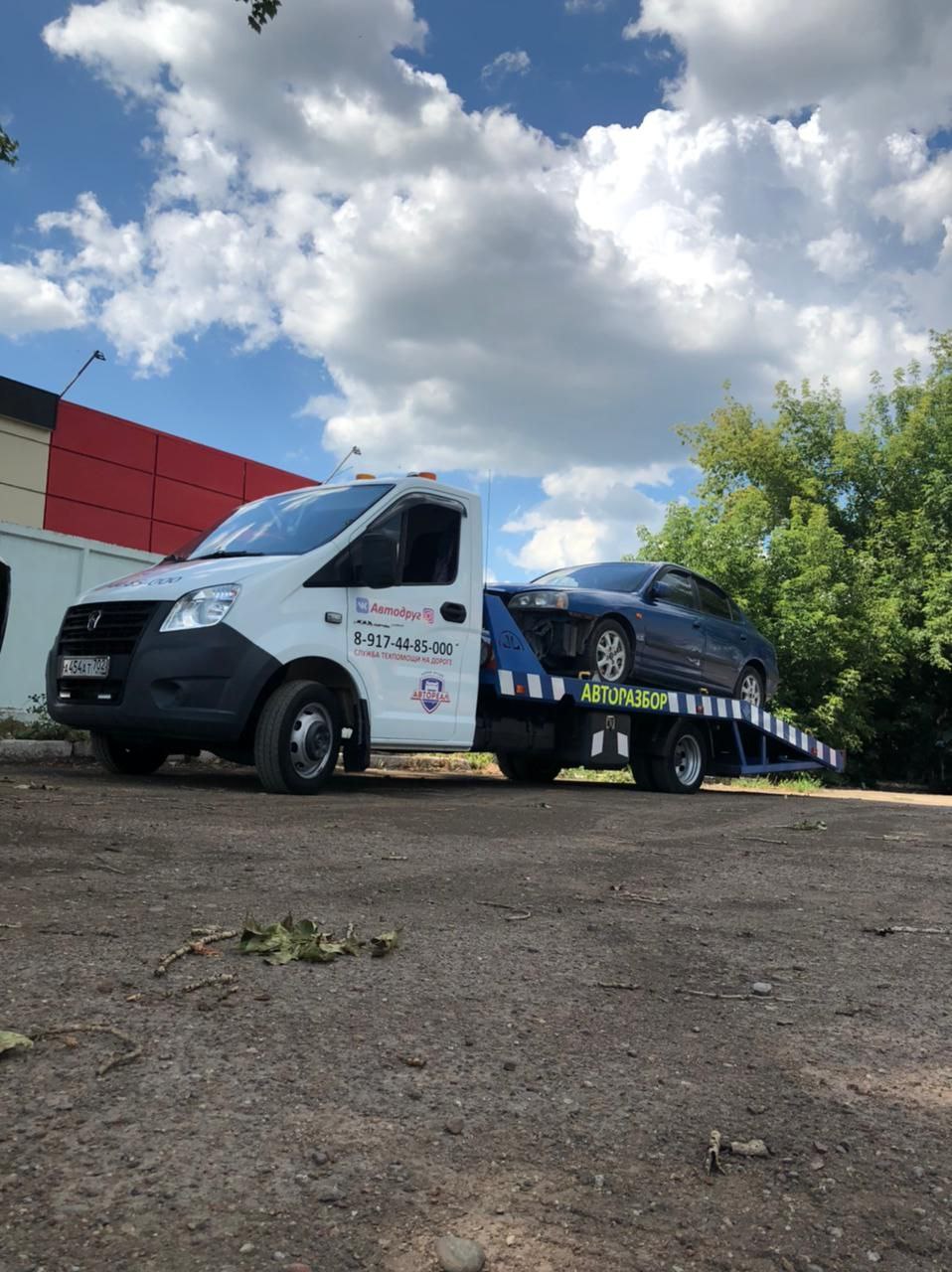 Белая Газель Next с легковым автомобилем на платформе